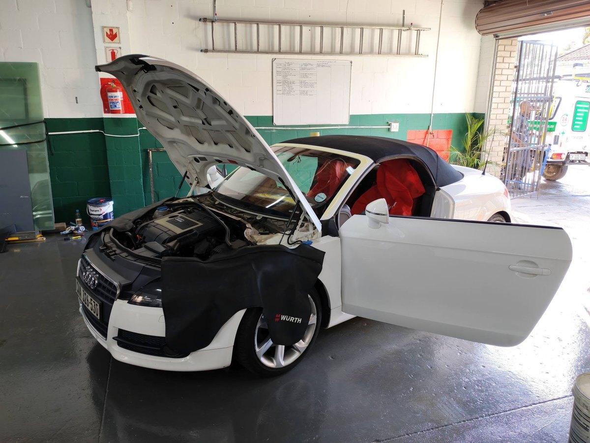 Black and white Audi with open hood and driver door in a repair garage with red interior visible