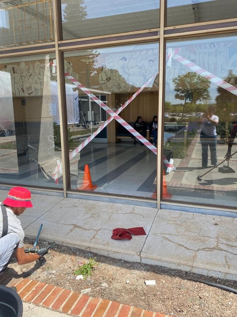 Large commercial shopfront glazing being replaced for a Brackenfell business, with red and white barrier tape crossed over the panes, an orange safety cone marking the work area and the street reflected in the glass during the replacement.
