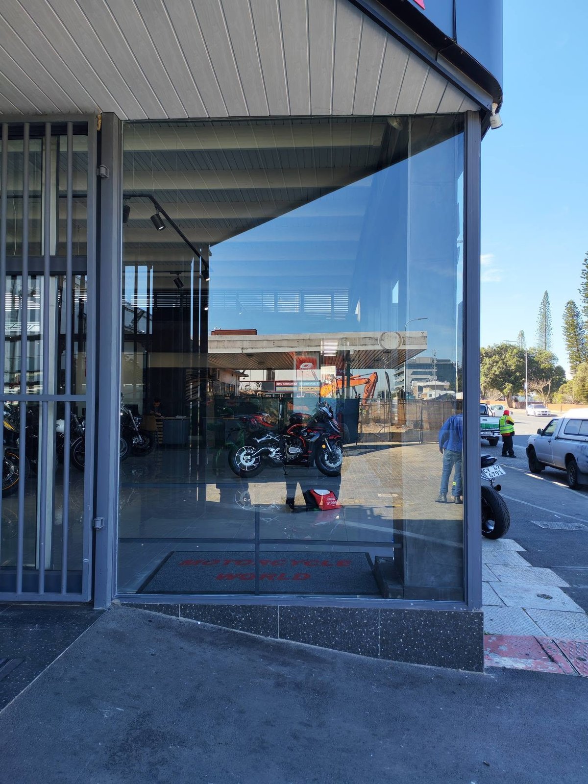 Modern motorcycle showroom with large glass storefront displaying a blue motorcycle inside, metal canopy overhead, clear day
