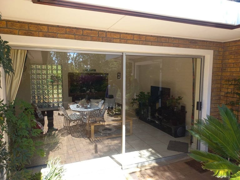 Newly fitted sliding glass doors in an Oranjezicht brick home, opening onto a tiled patio with potted plants and indoor living room visible through the clear glass.
