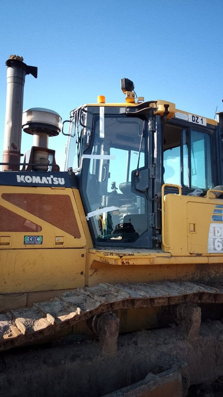 Yellow Komatsu excavator on sandy ground with its new cab glass fitted under a clear blue sky.