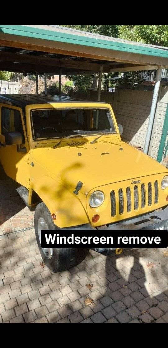 Yellow Jeep parked under a carport with windshield removed, showing interior modification work