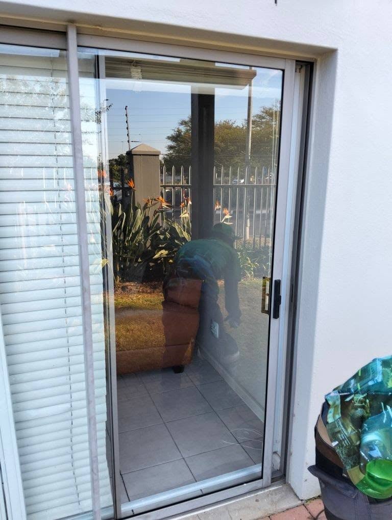 Newly fitted glass sliding door with white aluminium frame opening to an outdoor patio with potted plants and a white security fence