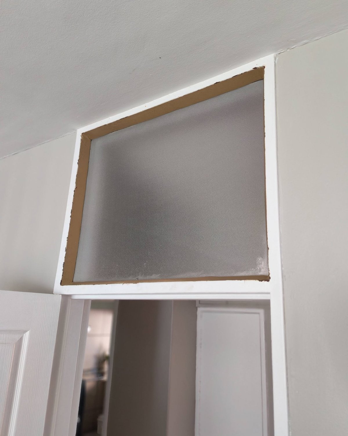 White-framed wall-mounted cabinet with brown wooden trim and gray interior panel installed above a doorway