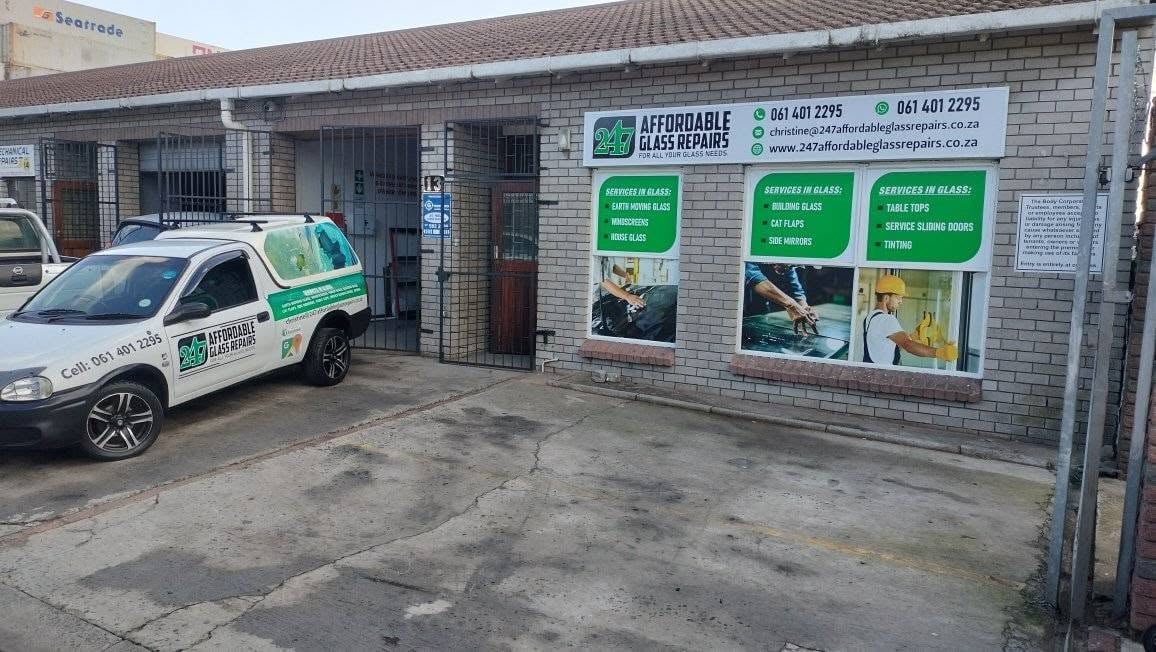 The 247 Affordable Glass Repairs workshop and office at Beacon Micro Industries, Beaconvale — white and green service van parked in the driveway next to the brick building with the full-colour services-in-glass shopfront signage.
