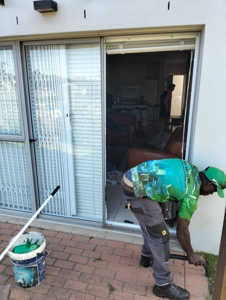 247 Affordable Glass Repairs worker in a green safety vest and cap carrying materials through the open sliding door into a residential lounge during a glass replacement.