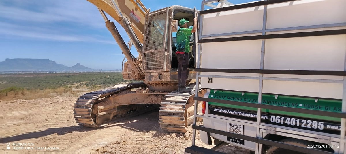 Excavator with tracks loading dirt into an open-bed truck on arid landscape with mountains in background