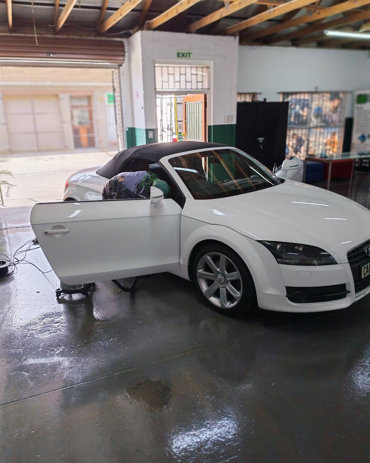 White Audi TT convertible with open drivers door in an industrial warehouse garage setting