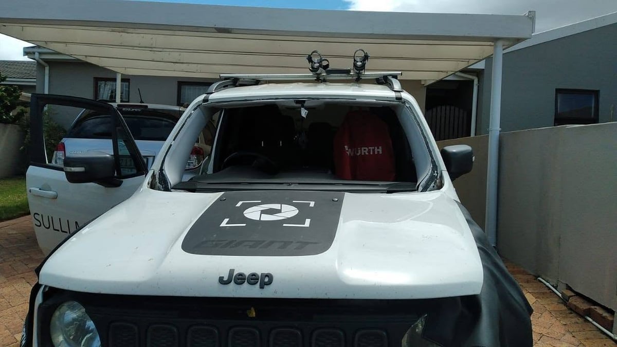 White Jeep vehicle parked in driveway with roof rack and dark hood decal