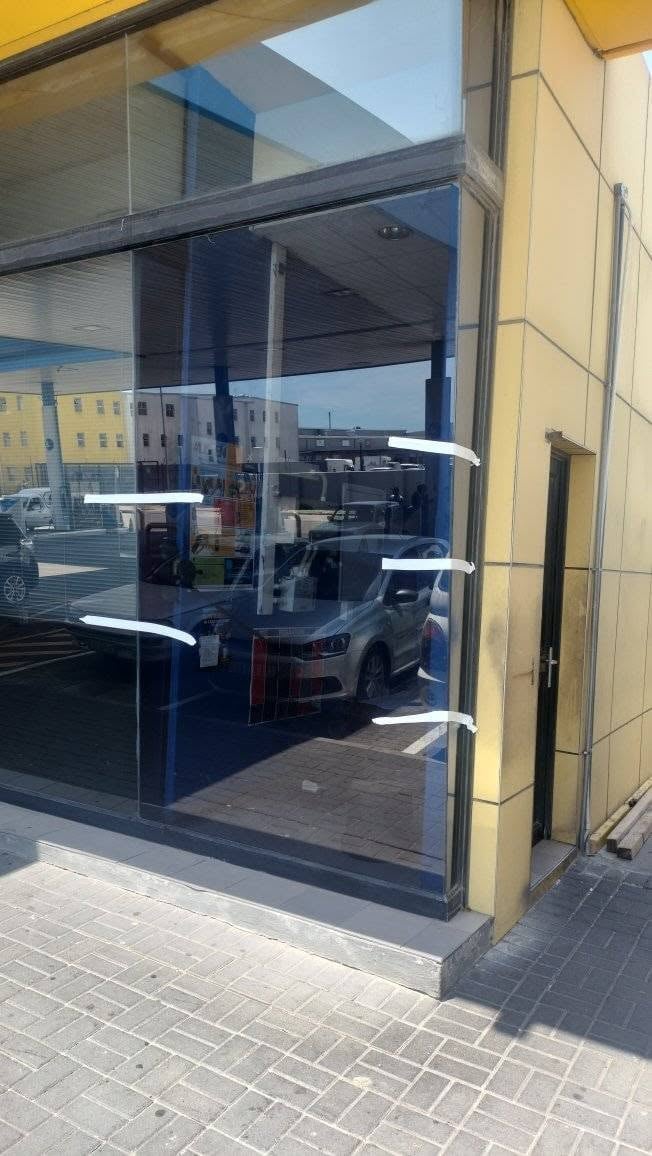 Modern storefront with large glass doors and windows showing parked cars inside, yellow building facade, and brick pavement