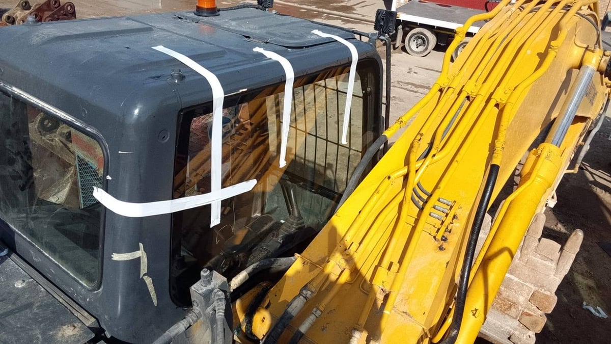 Dark blue earthmoving vehicle cab with white roof straps next to bright yellow hydraulic construction equipment in an outdoor storage area