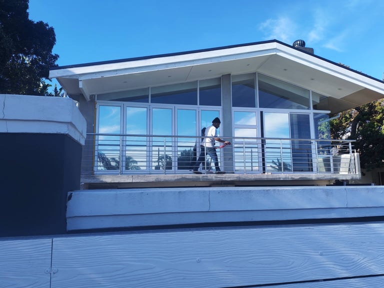 Newly fitted aluminium and glass windows, sliding doors and balustrades on a modern Vredehoek home, with a person standing on the timber deck under a clear blue sky.