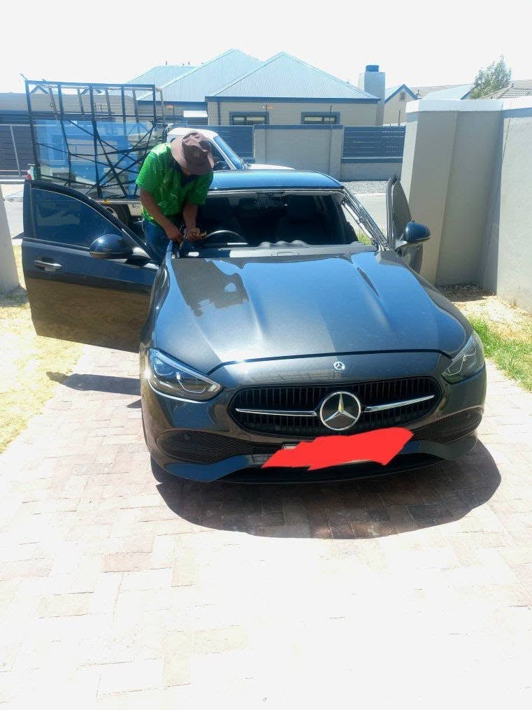 Man in green shirt working on black Mercedes-Benz with door open in residential driveway