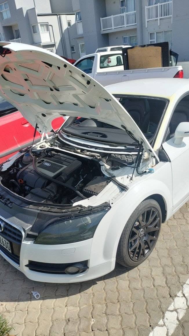 White car with open hood displaying engine in parking lot with residential buildings
