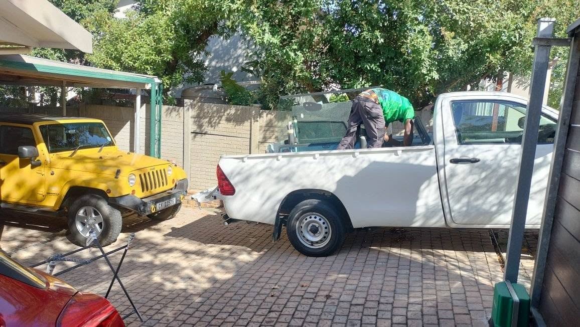 White pickup truck parked in driveway with yellow jeep and outdoor furniture visible in residential setting