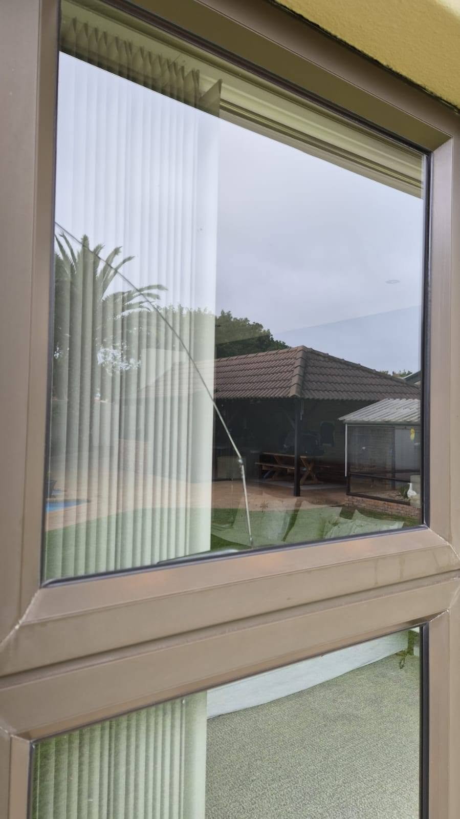 Window view of a patio and brick building with vertical blinds visible on the glass panes