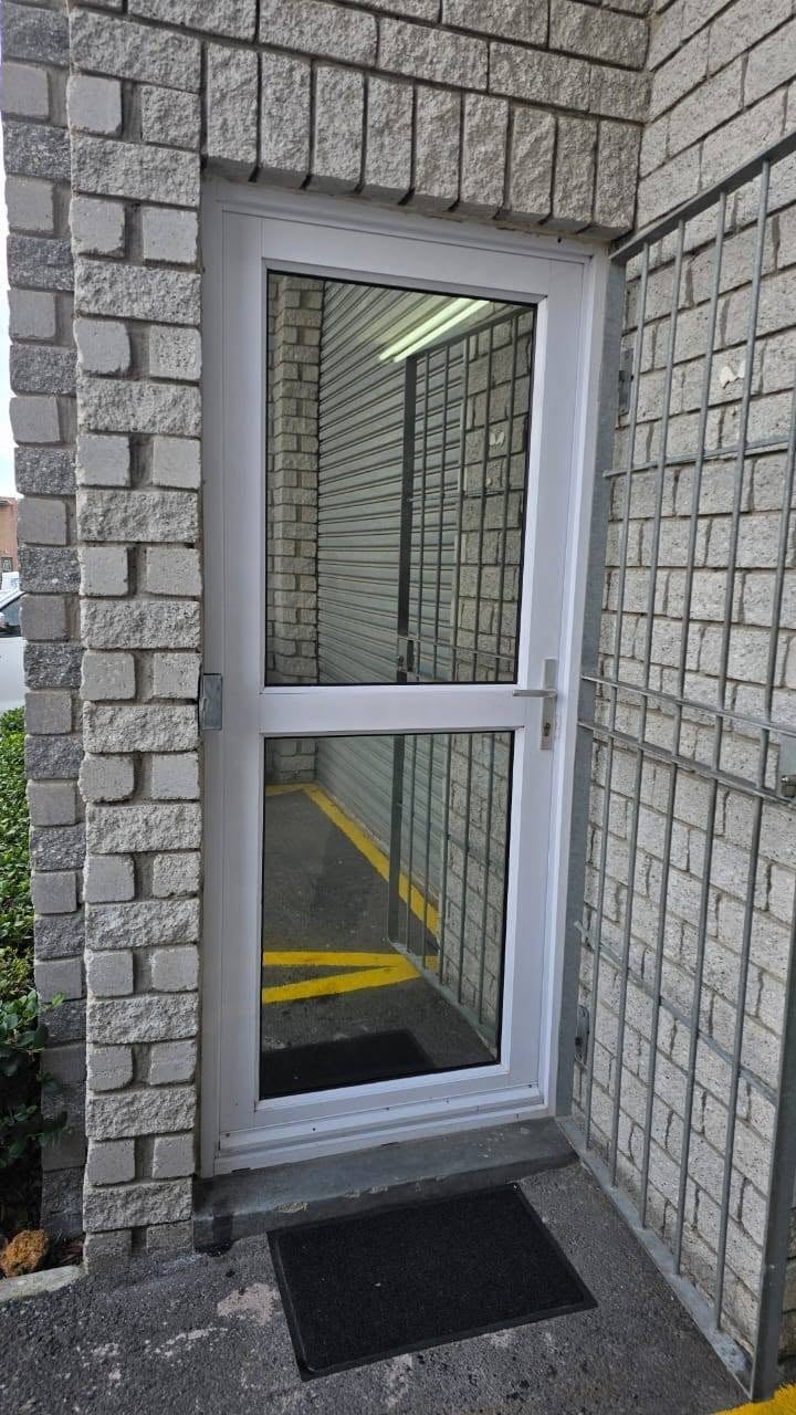 White aluminum glass door entrance set in gray brick wall with black mat on concrete threshold
