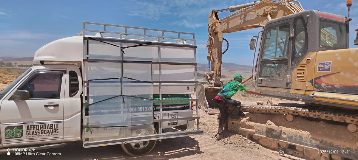 Affordable Glass Repairs service van parked next to a yellow excavator on a sandy site with a technician servicing the cab glass