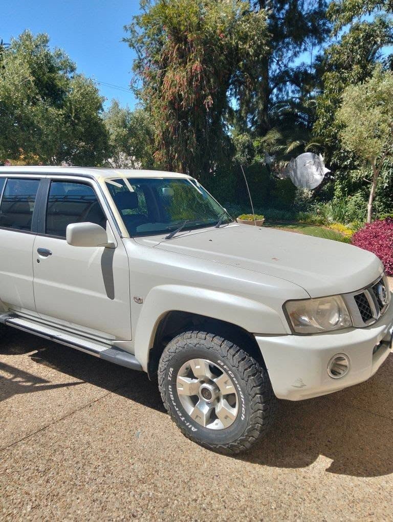 White SUV parked on gravel driveway with trees and landscaping in background on sunny day