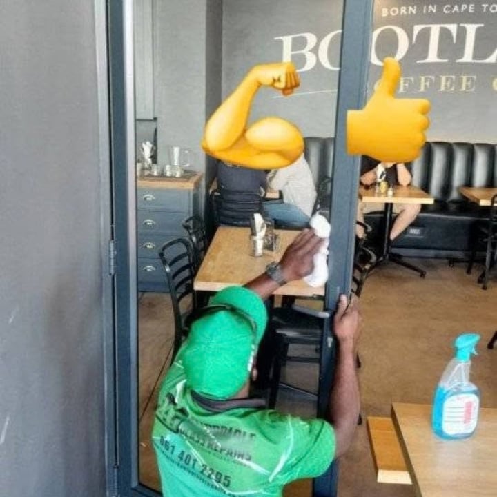 247 Affordable Glass Repairs technician in a green uniform and cap installing a new glass door panel at a Cape Town coffee shop, with the shop's 'BORN IN CAPE TOWN COFFEE' signage visible through the glass.