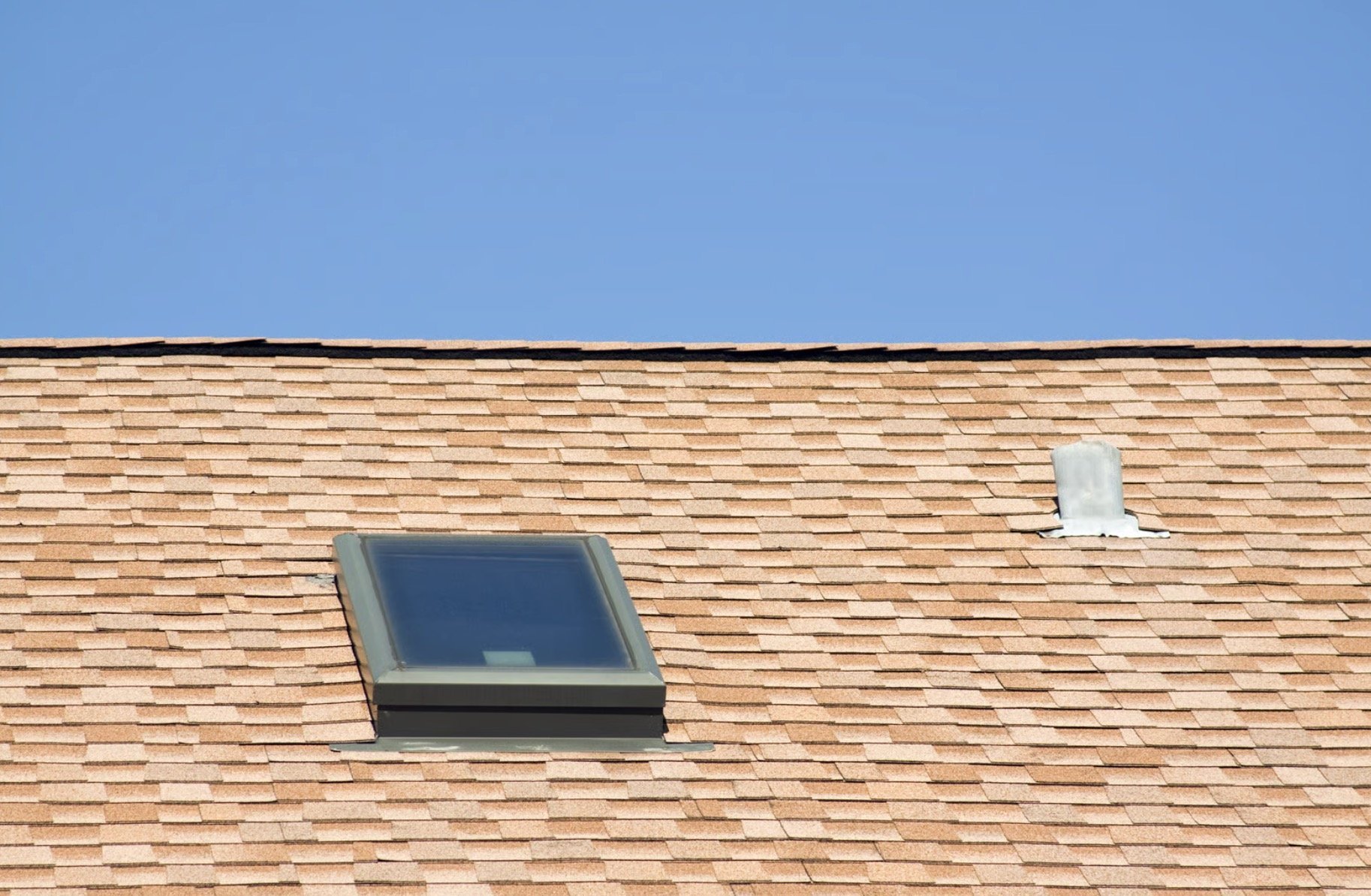 Skylight and roof vent on a brick shingled roof against a blue sky