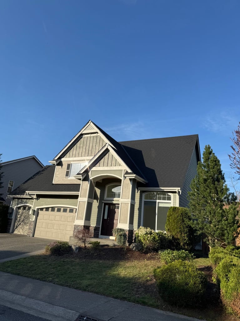 Two-story residential house with cream and dark trim, pitched roof, arched entryway, and attached garage under blue sky