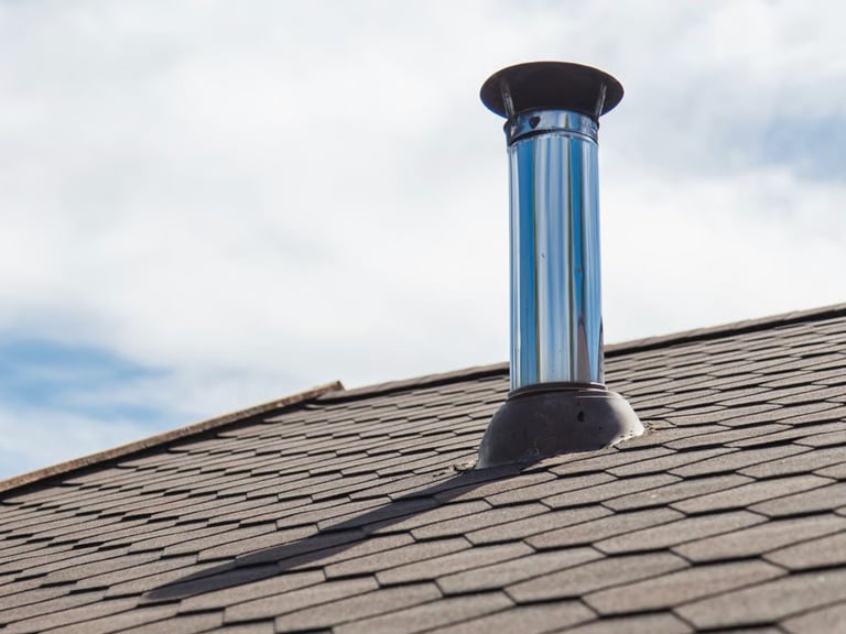 Blue metal chimney with black cap installed on gray asphalt shingled roof against cloudy sky