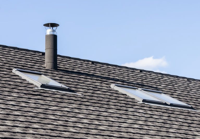 Asphalt shingle roof with metal chimney and installed skylights against a blue sky