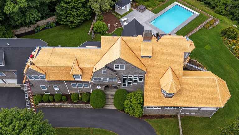 Aerial view of large residential home with new roof installation and swimming pool surrounded by green landscaping.