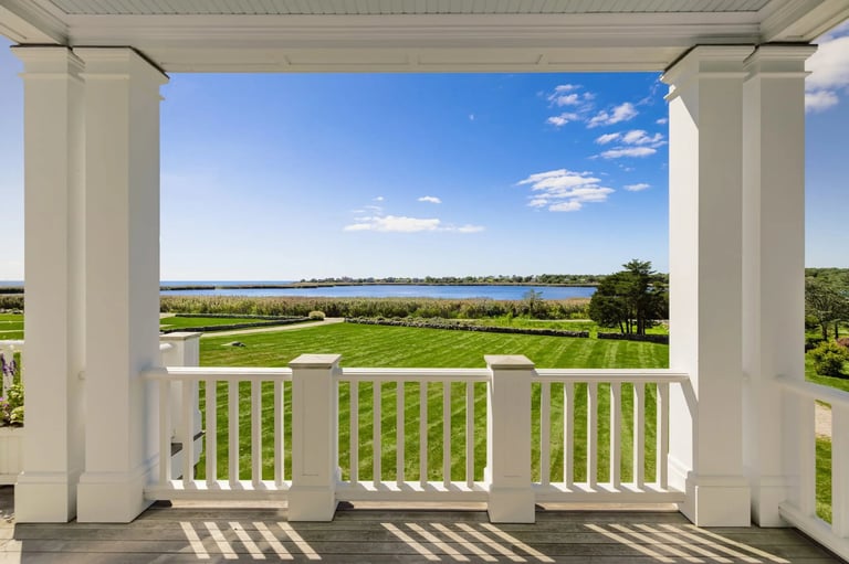 View from a white columned porch overlooking a calm waterfront with green lawns and blue sky