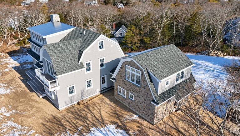 Aerial view of a residential property with white and gray houses, bare trees, and patches of snow in winter.