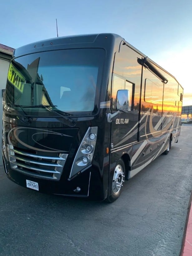 Black Outlaw class A motorhome parked in lot at sunset with reflective graphics and chrome details