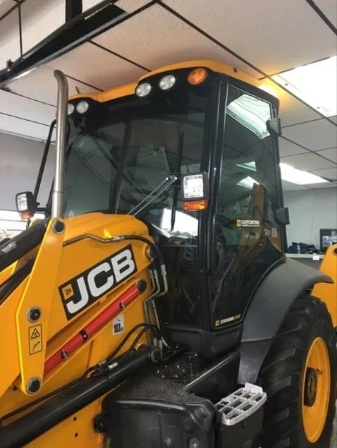 Close-up of yellow JCB telehandler cab showing open door, windshield, and control panel inside warehouse