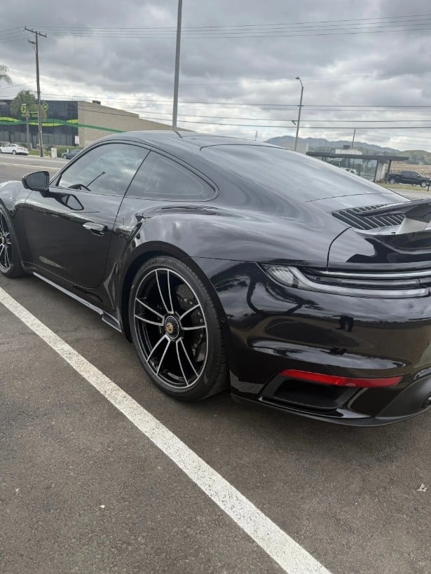 Black sports car parked in lot with mountains visible in background under cloudy sky