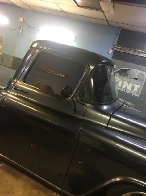 Classic black pickup truck parked in garage with open door and window visible