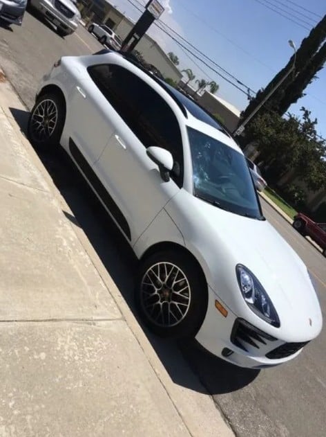White Porsche parked on a driveway, viewed from above at an angle, with alloy wheels and clear sky visible