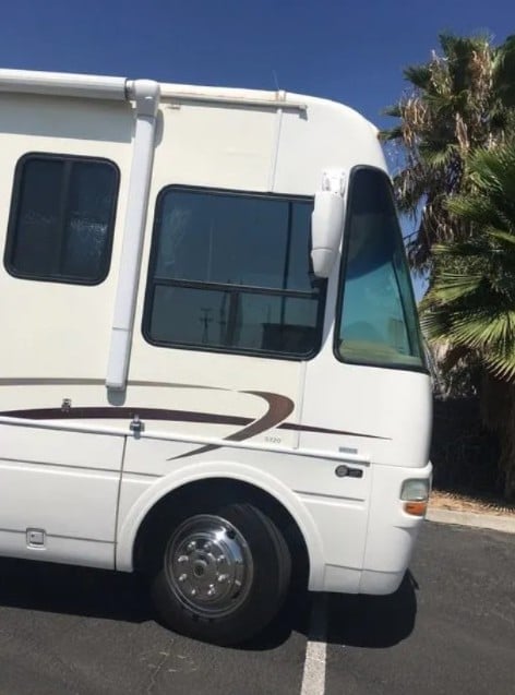 White motorhome RV parked outdoors with palm trees visible in background under clear blue sky