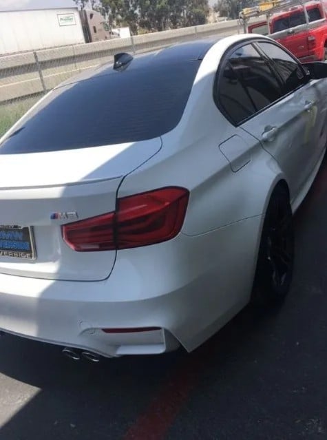 White BMW sedan parked on highway, rear view showing taillights and license plate