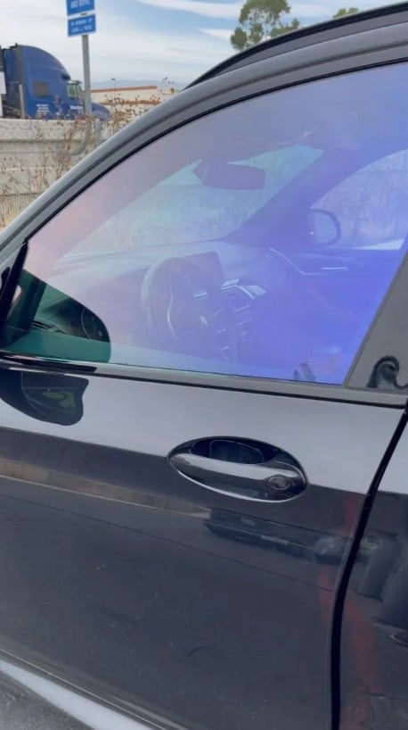 Car door with purple-tinted window film, parked on street with buildings and trees visible in background