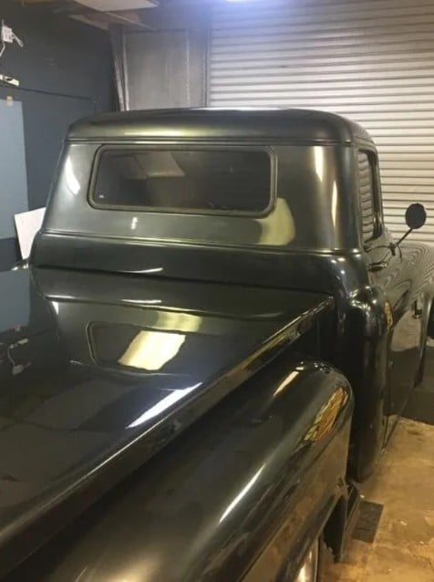 Vintage black truck with rounded cab parked in a garage under fluorescent lighting