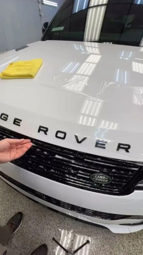 White Range Rover hood being polished with yellow microfiber cloth in a garage