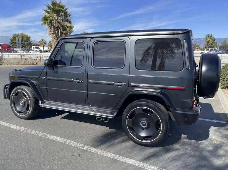 Black Mercedes-Benz G-Class SUV parked in lot with palm trees in background, side view