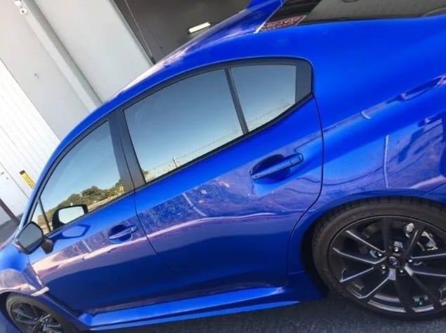 Bright blue sports car side profile showing sleek design, tinted windows, and dark alloy wheels parked near building