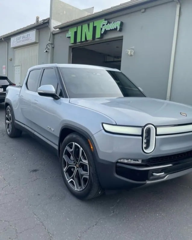 Silver electric truck parked in front of a window tinting shop building
