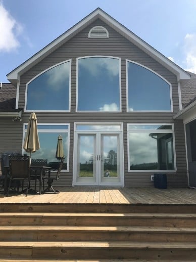 Modern gray house exterior with large arched window, glass patio doors, and wooden deck with outdoor furniture