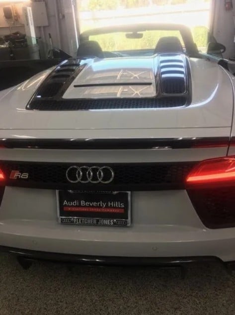 White Audi R8 convertible viewed from behind, showing open roof, red taillights, and dealership plate at Audi Beverly Hills