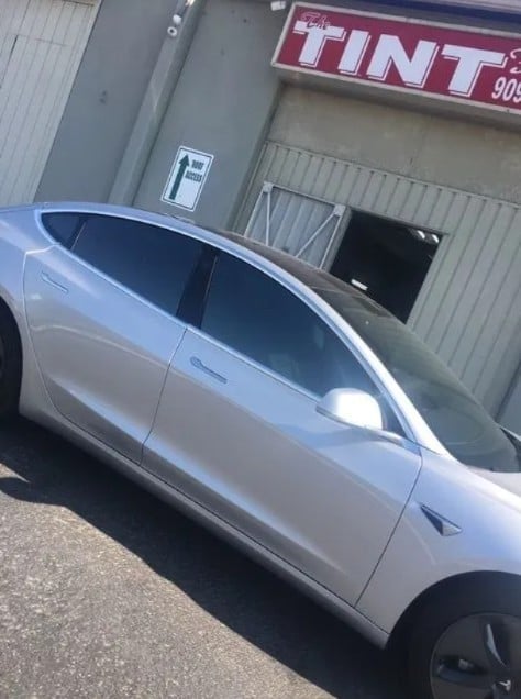 Silver car with dark tinted windows parked outside a tint shop storefront
