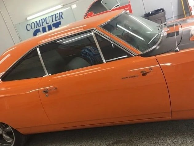 Vintage orange car with doors open, parked indoors near a computer store sign