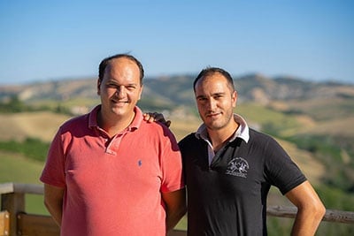 Two men smiling at camera with rolling hills and countryside landscape in background