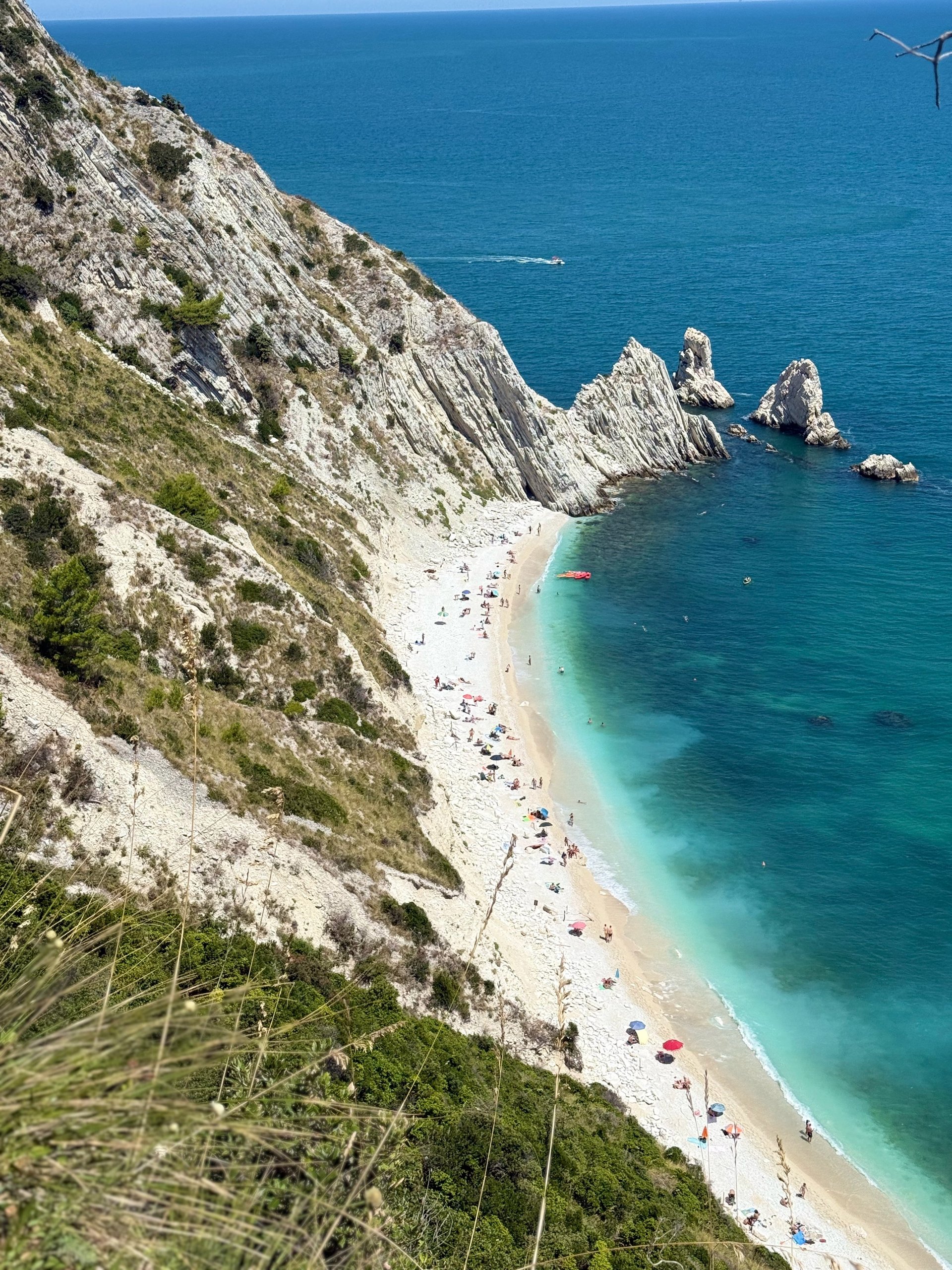 Aerial view of a white pebble beach nestled below dramatic chalk cliffs with turquoise waters and rock formations offshore